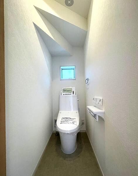 小窓から自然光が入り明るい印象のトイレです。シンプルなデザインで清潔感があります。天井の形状も特徴的で空間にアクセントを加えています。壁リモコンの設置で使い勝手にも配慮されています。