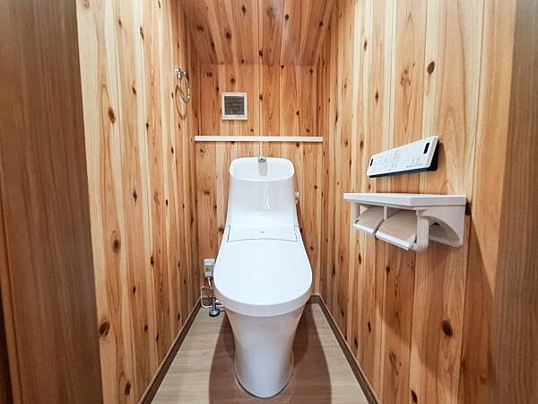 温かみのある木目調の壁が特徴的なトイレです。白を基調とした設備が清潔感を演出しています。収納やリモコンも使いやすい位置に配置されています。