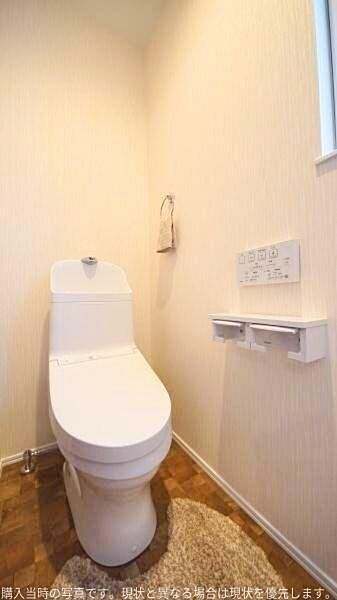 すっきりとしたデザインのトイレです。壁付けのリモコンが設置されており操作も簡単です。明るい内装が清潔感を演出します。窓付きで換気も確保しやすいです。