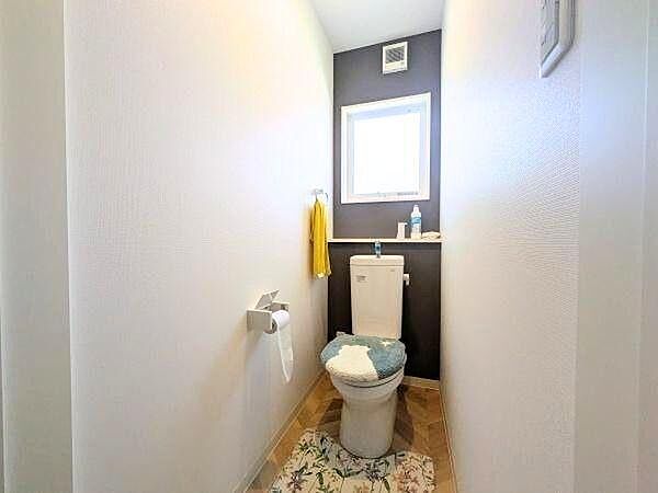 明るい光が差し込む空間で清潔感のあるトイレです。壁のアクセントカラーが印象的です。収納スペースも備わっています。シンプルで使いやすいデザインです。