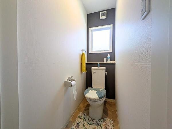 明るい光が差し込む空間で清潔感のあるトイレです。壁のアクセントカラーが印象的です。収納スペースも備わっています。シンプルで使いやすいデザインです。