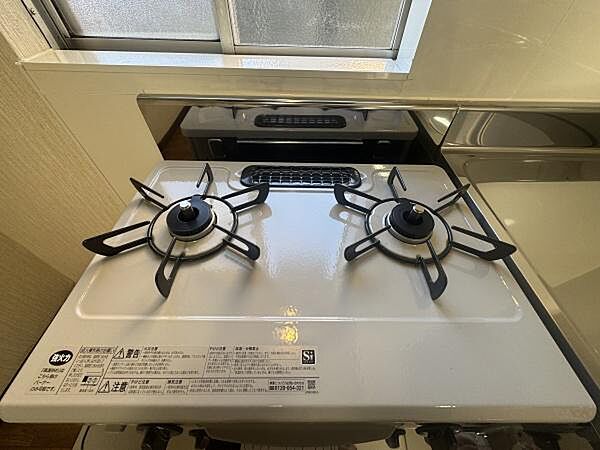 明るいキッチン空間に設置されたガスコンロはシンプルで使いやすいデザインです。2口タイプのため調理が効率的にできます。お手入れしやすい素材が採用されているのもポイントです。窓からの採光で換気も良好です。