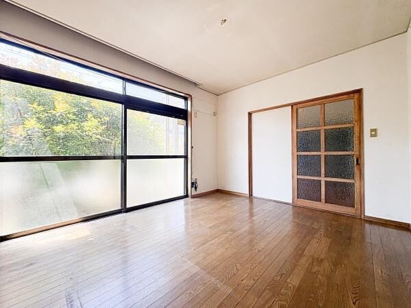 大きな窓から豊かな自然光が降り注ぐ洋室です。落ち着いた色合いのフローリングが特徴的です。シンプルな壁面とガラス扉が開放感を演出します。