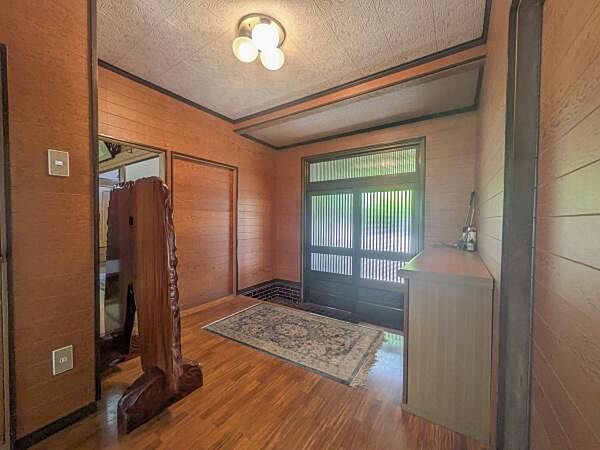 木目調の壁と床が温かみを感じさせる玄関です。広々とした空間で収納も確保されています。大きな窓から自然光が入り明るい印象です。照明の配置も工夫されており落ち着いた雰囲気を演出しています。