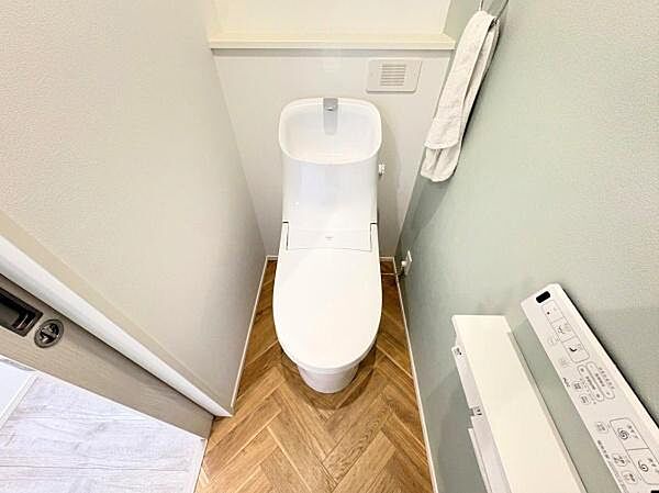 白を基調とした清潔感のあるトイレです。木目調の床が空間に温もりを与えます。手洗い一体型のデザインが特徴です。収納スペースも実用的です。