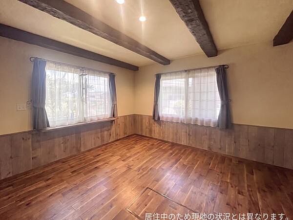 木目調のフローリングと梁が特徴的な洋室です。二面採光で室内が明るく快適な空間が広がっています。窓にはカーテンとレースが備え付けられておりプライバシーにも配慮されています。