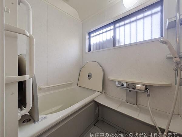 明るい窓が設けられたバスルームです。手すりがあり安心して利用できます。浴槽はゆったりとした設計となっています。収納スペースも備わっています。壁面は清潔感のある色合いです。