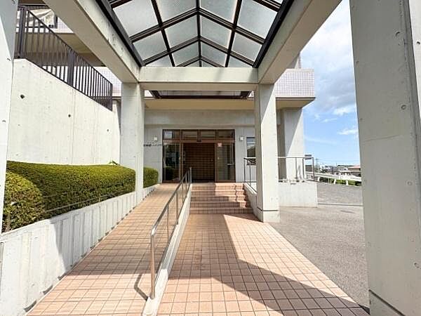 広々としたエントランスが開放感を与えます。屋根付きのアプローチで雨の日も安心です。スロープが設けられており利便性が高いです。植栽がさりげなく配置されています。