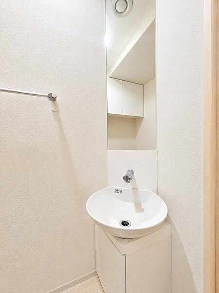 清潔感のあるシンプルな空間が広がるトイレです。洗面台が設置されており使いやすさにも配慮されています。淡いカラーの壁が明るい印象を与えます。ミラー付きで日常の身だしなみチェックにも便利です。