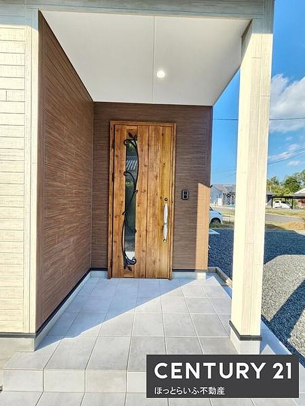木目調の玄関扉が目を引く外観です。軒下空間がしっかり確保されており雨の日でも安心して出入りできます。タイル貼りのアプローチが清潔感を演出しています。