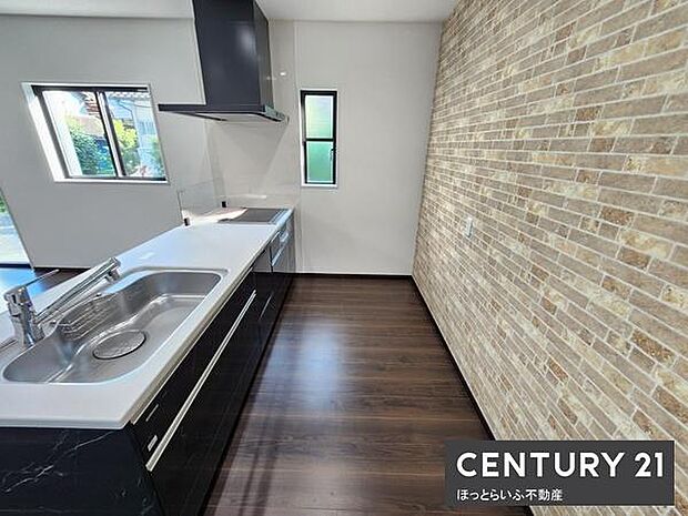 レンガ調のアクセントウォールが目を引くキッチンです。シンクや調理スペースがゆったりと配置されています。窓からの採光で明るい雰囲気です。床のダークブラウンが落ち着いた印象を与えます。