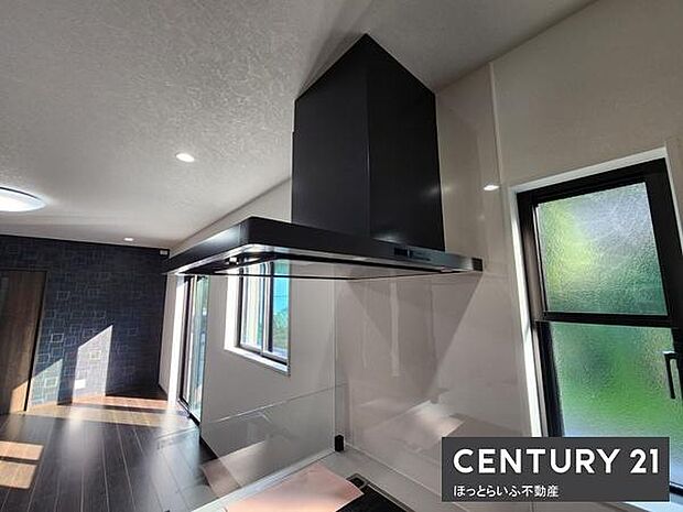 キッチンにはモダンなレンジフードが設置されており室内に開放感があります。窓から自然光が入りやすく明るい印象の空間です。ダークカラーの床材が全体を引き締めスタイリッシュなデザインが特徴です。