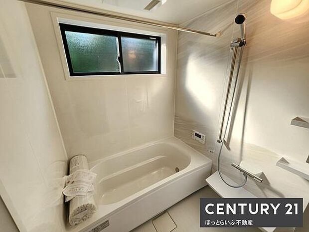 窓付きで自然光が差し込むバスルームです。浴槽の形状が使いやすく壁付けシャワーも設置されています。清潔感のある白を基調としたデザインです。浴室乾燥用のバーも備え付けです。収納棚も便利に利用できます。