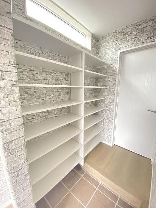 玄関スペースに豊富な収納棚が設けられており整理しやすい設計です。上部の窓から自然光が差し込み明るい空間が広がります。壁面は石目調のデザインがアクセントとなっています。