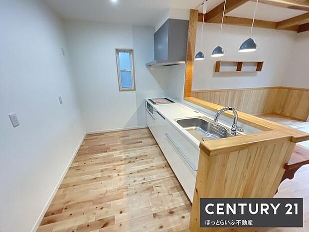 明るい色合いのフローリングと木目調のカウンターが調和したキッチンです。天井の照明が空間にアクセントを加えています。収納スペースも充実しており使いやすさが感じられます。