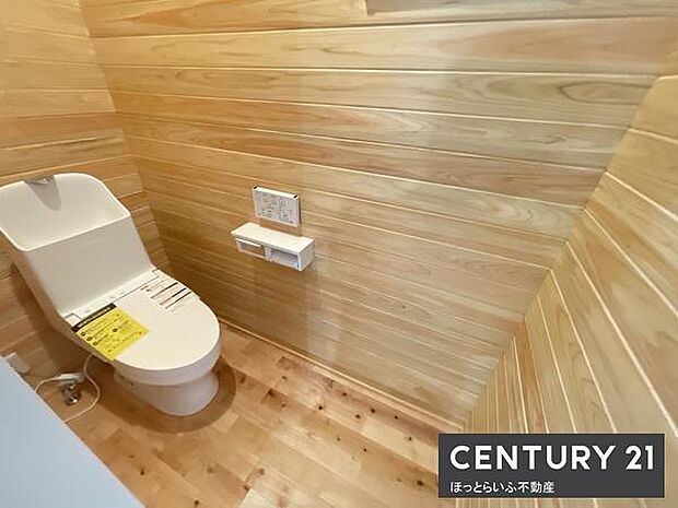 木目調で統一された内装が特徴的なトイレです。温かみのある空間が清潔感を感じさせます。壁や床のデザインがナチュラルな雰囲気を演出しています。ペーパーホルダーや操作パネルも設置されています。