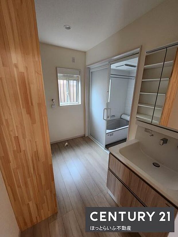 洗面台と収納棚がシンプルで使いやすい印象です。大きな鏡が備えられており毎日の身支度にも便利です。窓から自然光が差し込み明るい空間が広がっています。床材のデザインも落ち着いた雰囲気を演出しています。