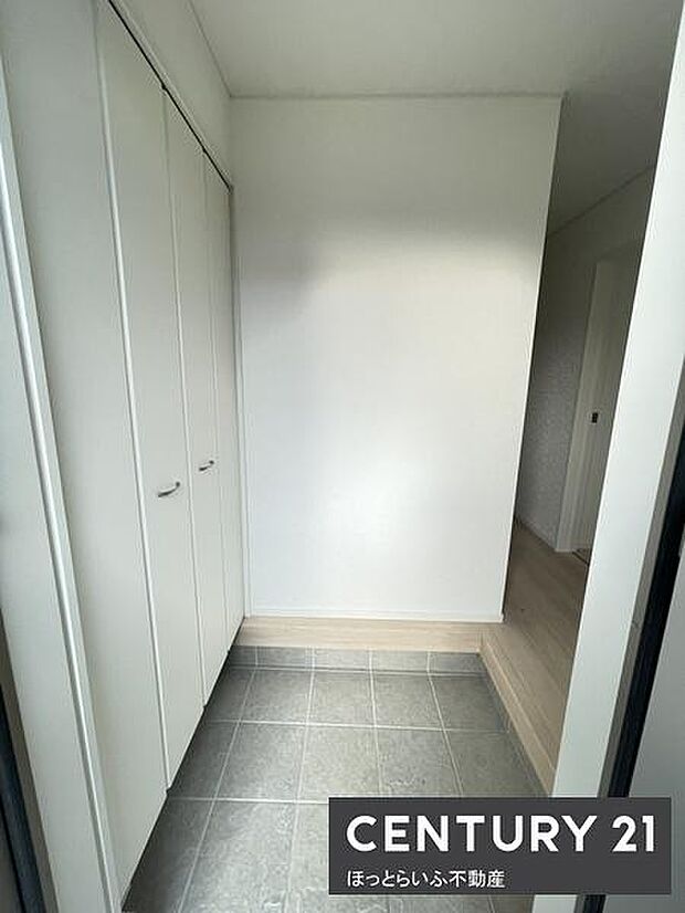 白を基調とした清潔感のある玄関です。広めのスペースが確保されており収納も豊富です。タイル床が使いやすさを感じさせます。室内との段差も低めで快適に出入りできます。明るい空間が印象的です。