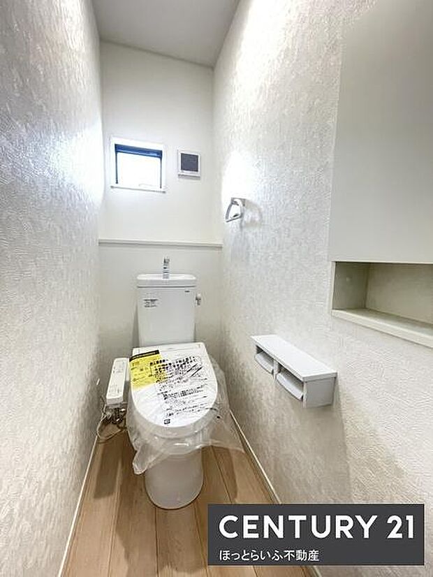 窓があり換気に配慮された明るいトイレです。収納スペースも確保されペーパーホルダーが2連で便利に使えます。床は木目調で清潔感があります。照明もしっかり確保されており快適な使用感につながります。