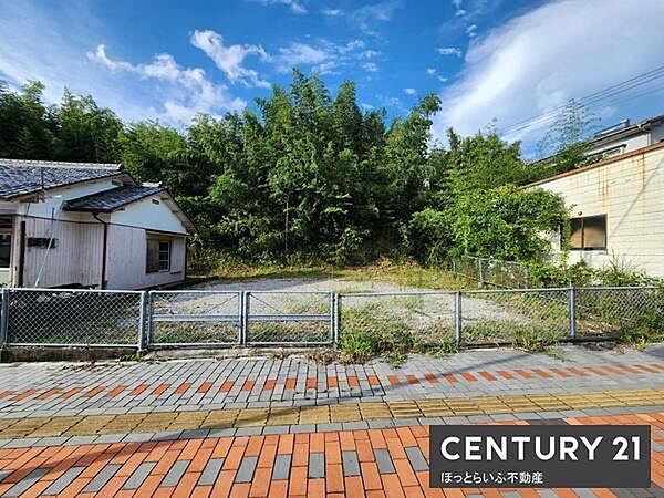 青空と緑豊かな木々に囲まれた現地土地写真です。整った形状の土地で様々な用途に活用しやすい雰囲気です。前面道路の舗装も整えられており利便性を感じられます。