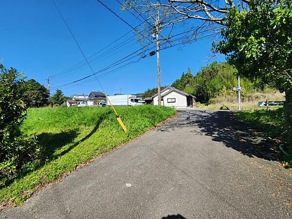 前面道路が広く車両の出入りがしやすい印象です。周囲は落ち着いた雰囲気で自然も感じられます。晴れた日の空の青さが印象的です。電柱や電線も整然と配置されています。街路樹の緑がアクセントになっています。