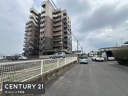 しっかりとした造りのマンション外観で存在感のある建物です。ゆったりとした道路が建物前に広がっており駐車スペースも十分に確保されています。周囲は開放感があり落ち着いた環境が感じられます。