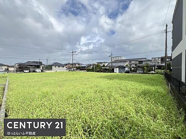 広々とした現地土地写真です。周囲には住宅が立ち並び落ち着いた雰囲気が感じられます。日当たりが良く開放感のある景観が魅力です。敷地の形が整っており様々な活用が考えられます。