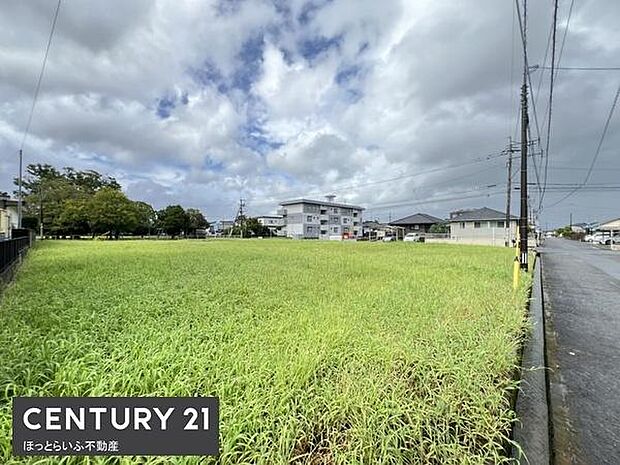 広々とした敷地が特徴の現地土地写真です。周囲には住宅や建物が並び穏やかな街並みに調和しています。道路にも面しており利便性が感じられる環境です。開放感が伝わる現地の様子が確認できます。