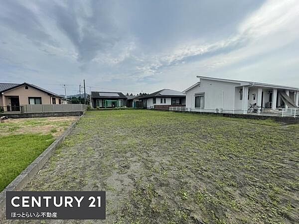 ゆったりとした現地土地写真です。周囲には住宅が建ち並び整った街並みが広がっています。道路や近隣の様子も確認でき敷地の広がりが感じられる一枚です。空が広く開放感を味わえます。