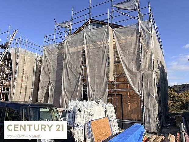 木造住宅の工事現場です。足場や養生シートが設置されており安全面にも配慮されています。現場の整理整頓が行き届いている印象です。周辺には自然を感じられる環境も広がっています。