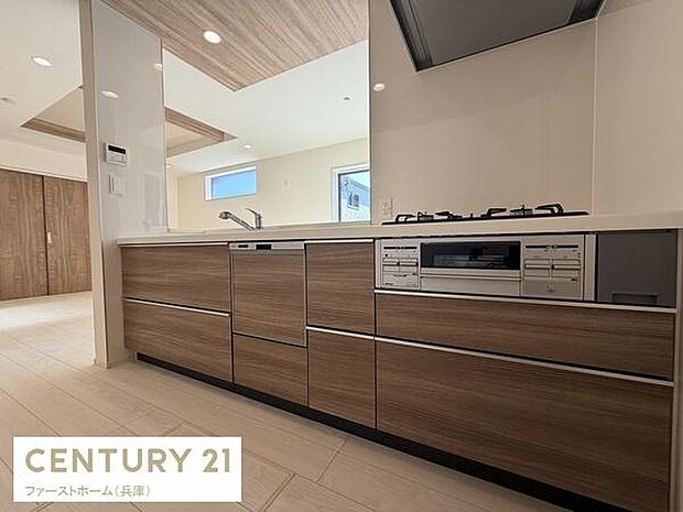 木目調のパネルが印象的なキッチンです。ワイドな作業スペースが特徴的です。明るい室内で開放感も感じられます。収納も豊富に備わっています。フラットなカウンターが設置されています。