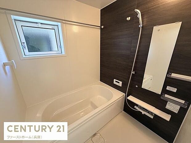 黒を基調とした壁面が洗練された印象を与えます。ゆったりとしたバスタブが設置されています。窓が設けられており換気や採光にも配慮されています。浴室乾燥機の操作パネルも設置されています。