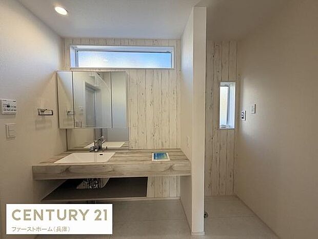 洗面台は横幅にゆとりがあり使いやすい設計です。ミラーキャビネット付きで収納スペースも確保されています。木目調のパネルがやわらかな印象を与えます。上部には横長の窓があり自然光が差し込みます。