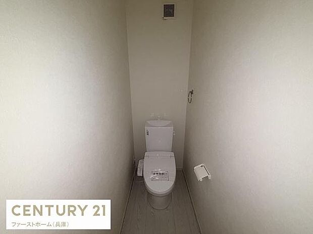 シンプルなデザインのトイレが印象的です。白を基調とした空間で清潔感を感じられます。ペーパーホルダーも壁面に設置されています。換気設備も備わっています。