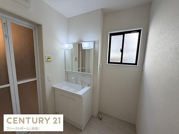 シンプルで清潔感のある洗面台が設置されています。明るい照明付きで朝の身支度も快適に行えます。窓があり換気にも配慮されています。収納力のあるキャビネットも備えています。