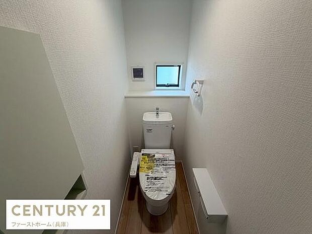 落ち着いた色合いの壁紙と床材が特徴のトイレです。コンパクトながらも設備が整っており窓があるため換気も可能です。収納スペースも確保されていて機能的です。手洗い一体型便器で使いやすさが考慮されています。