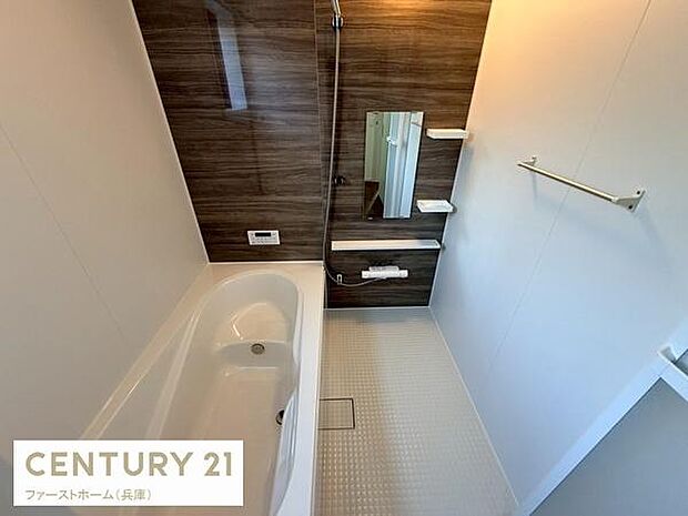 木目調パネルがアクセントのバスルームです。鏡や棚も設置されており使い勝手に配慮されています。浴槽と洗い場がゆったりとした造りになっています。全体的に明るい印象の室内です。