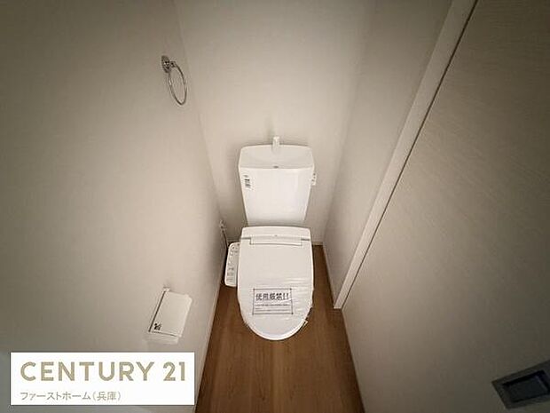 シンプルですっきりとしたデザインのトイレです。床材が明るく清潔感を感じさせます。ペーパーホルダーやタオルリングが設置されています。壁や床の配色が落ち着いた印象を与えます。