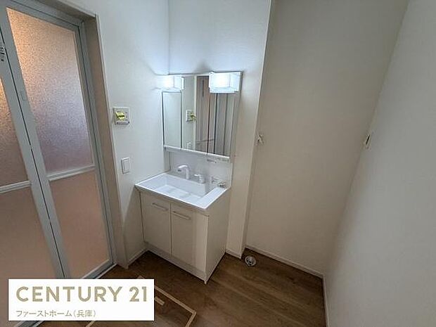 シンプルなデザインの洗面台が設置されています。鏡の両端に照明があり明るく使いやすい空間です。木目調の床材が落ち着いた雰囲気を演出しています。収納スペースも備わっており整理整頓に便利です。