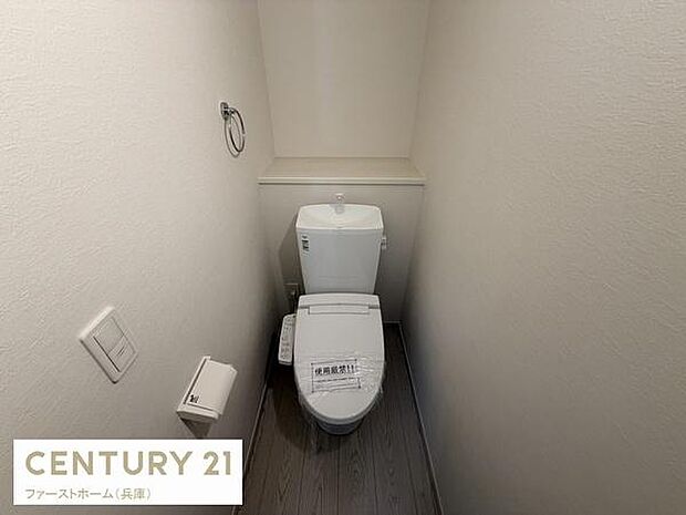 シンプルなデザインのトイレ空間です。壁紙や床材が落ち着いた色合いでまとめられています。トイレットペーパーホルダーやタオルリングも設置されており使いやすさが感じられます。収納スペースも確保されています。