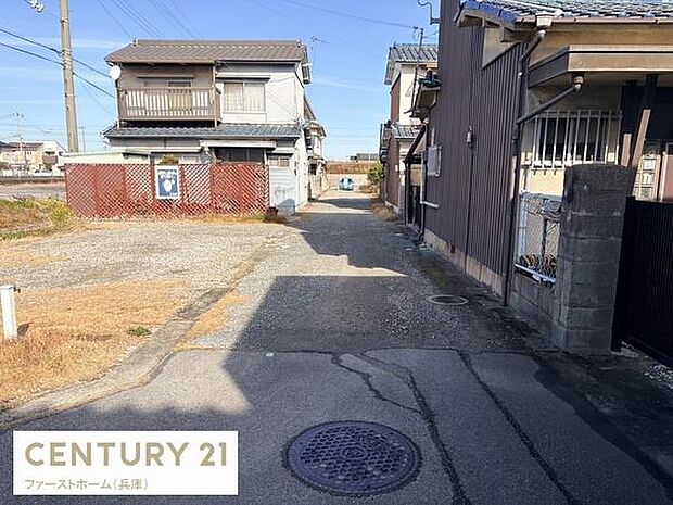 現地の前面道路は舗装されており周囲も住宅が立ち並ぶ落ち着いた環境です。車の出入りもしやすい道幅となっています。周辺の様子がしっかりと確認できる写真です。現地の状況がわかりやすく安心感があります。