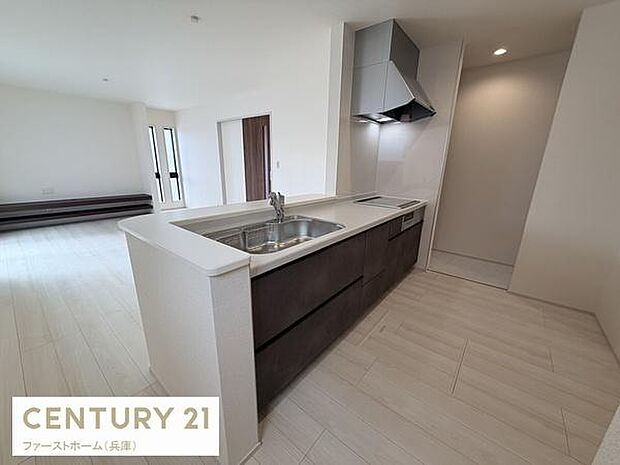 広々としたキッチンは開放感があり作業スペースがしっかり確保されています。洗練されたダークカラーの収納が特徴的です。換気フードやシンクなど機能性も感じられるデザインです。