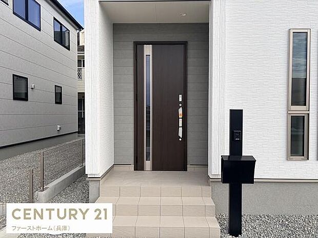 玄関は落ち着いた色合いでシンプルながら印象的なデザインです。タイル張りのアプローチが清潔感を演出しています。モダンな雰囲気の玄関ドアが建物全体に調和しています。