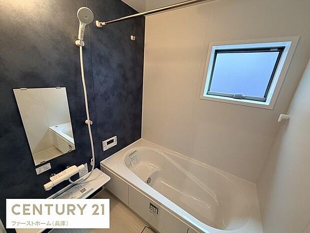 モダンなアクセントクロスが印象的な浴室です。窓があり自然光が入るため明るい雰囲気があります。便利なシャワー設備とワイドな鏡が設置されています。浴槽もゆったりとした形状でリラックスできる空間です。