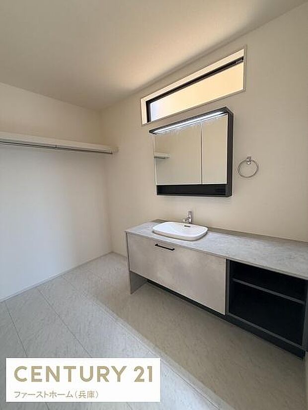 明るい洗面台が設けられており使いやすい空間が広がっています。ミラーキャビネットが設置されており収納にも配慮されています。天井近くの窓から自然光が入り洗面所全体が開放的な印象です。