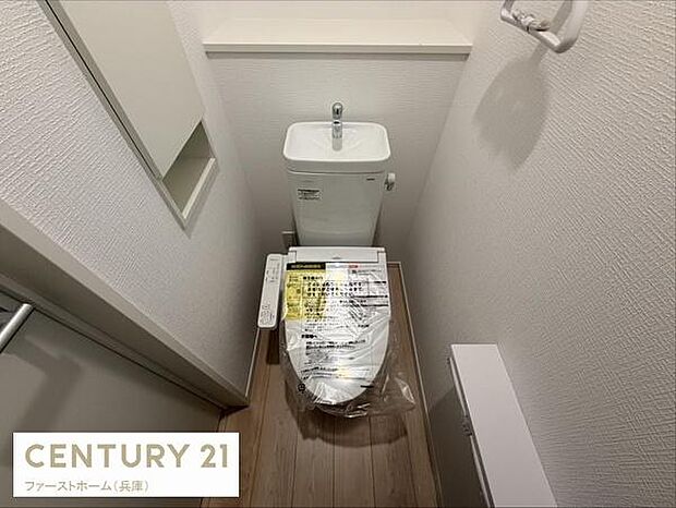 シンプルで清潔感のあるトイレ空間です。壁紙や床材も落ち着いた色合いで統一されています。備え付けの棚も便利にご使用いただけます。換気に配慮された設計となっています。使い勝手の良いレイアウトです。