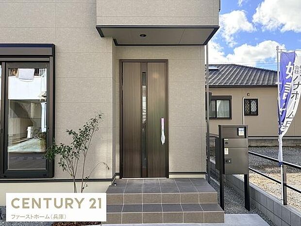 シンプルで洗練されたデザインの玄関が魅力的です。屋根付きのアプローチで雨の日も安心です。幅の広いタイルステップがゆとりを感じさせます。玄関横の植栽が外観にアクセントを加えています。