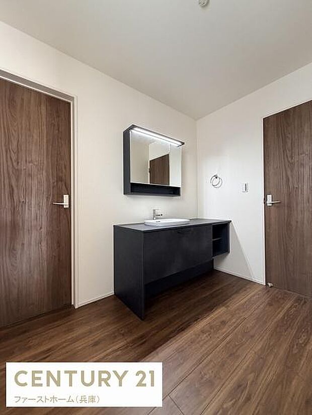シンプルなデザインの洗面台が配置されています。広々とした空間で毎日の使用にも便利です。木目調の床が落ち着いた雰囲気を演出しています。収納スペースも確保されています。清潔感のある洗面所です。