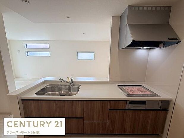 シンプルなデザインで統一されたキッチンです。木目調のパネルが空間に温かみを加えています。IHクッキングヒーターと換気扇が設置されており機能性も考慮されています。ダブルシンクで使い勝手も良好です。