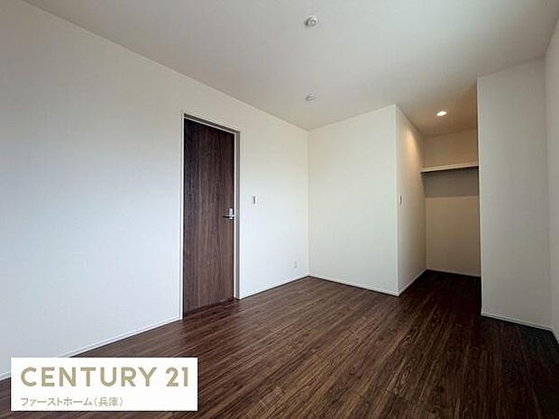 落ち着いた色合いのフローリングが印象的な洋室です。シンプルな壁と扉が空間をすっきりと見せます。収納スペースも備えられています。照明が室内を明るく照らします。広がりのある使いやすいレイアウトです。